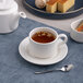 A warm white porcelain tea cup with a matching saucer, filled with tea and placed on a blue placemat.