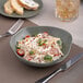 A bowl of Ariane Mist Green Dots porcelain pasta with vegetables and cheese on a table with a fork and knife.