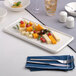 A rectangular warm white porcelain tray with assorted cheeses, nuts, and berries arranged on it.