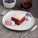 An Ariane porcelain plate with a slice of red velvet cake and a fork on a table.