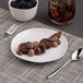 An Ariane Earth porcelain plate with a chocolate dessert and a bowl of blackberries on a table with a glass of juice.