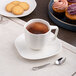 A white porcelain saucer with a cup of coffee and cookies on a table.