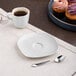 A white porcelain saucer with a cup of coffee and a cupcake on a table.