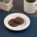 A white round porcelain plate with an embossed wide rim, holding two chocolate cookies.