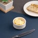 A small white embossed porcelain ramekin filled with butter cubes.