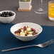 A warm white porcelain nappie bowl filled with salad, placed on a blue placemat with a fork nearby.