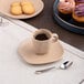 An Ariane dark sand dots espresso cup filled with coffee on a saucer with cookies.