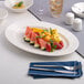 An oval wide rim porcelain platter in warm white, measuring 11 by 7 11/16 inches, displayed with assorted fruit.