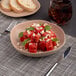 A dark sand dots porcelain plate with watermelon salad and a fork next to a glass of soda.