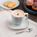A white porcelain cup filled with coffee sitting on a table with cookies.