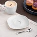 A plate with an Ariane Earth linen dots saucer and a cup of coffee with cupcakes on a table.