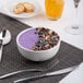 A white porcelain bowl filled with a purple smoothie, granola, blueberries, and coconut flakes.