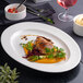 An oval white embossed wide rim platter with a gourmet meal served on it.