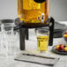 A black pinewood beverage dispenser stand holding a glass drink dispenser on a marble countertop.