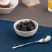 A small warm white porcelain bowl filled with blackberries, accompanied by a metal spoon.