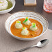 A white Ariane Tornado porcelain bowl filled with soup and dumplings.
