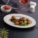 An oval white embossed wide rim platter holding roasted potatoes with garnish.