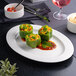 A white oval embossed wide rim platter holding three stuffed green bell peppers on a bed of red sauce.