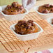 A square white oven-safe paperboard baking pan containing a sticky bun topped with pecans.