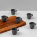 A group of Ariane charcoal grey porcelain espresso cups on a wooden board.