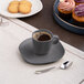 A cup of coffee on a Ariane Earth Charcoal Grey Dots porcelain saucer with cookies.