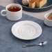 A round, warm white porcelain mug saucer with a wide rim.