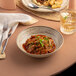 A white Ariane Tornado porcelain plate with food and a glass of wine on a table.