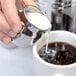 A person pouring milk from an American Metalcraft milk can into a cup of coffee.