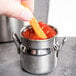 A person holding a small American Metalcraft milk can creamer filled with ketchup.