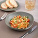 A bowl of salad with tomatoes and green onions on a table with a fork and knife.