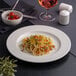 A white round embossed wide rim flat porcelain plate with a serving of pasta.