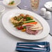 An oval wide rim porcelain platter in warm white, displayed with assorted Mediterranean appetizers.