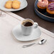 An Ariane Earth white porcelain espresso cup filled with coffee on a table with cookies.