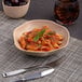 A bowl of pasta with sauce and basil in an Ariane Earth dark sand dots porcelain bowl.