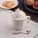 An Ariane porcelain mug of coffee with whipped cream and cookies on a counter.