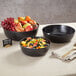 A large black round melamine serving bowl filled with assorted fresh fruit.