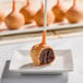 A pumpkin-flavored cake pop with orange coating and yellow sprinkles, partially eaten to show the chocolate cake interior, displayed on a small white plate.