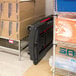 A black Rubbermaid convertible utility cart on a shelf with boxes and a carton.