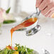 A stainless steel gravy boat being used to pour sauce onto a salad.