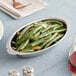 A stainless steel oval au gratin dish filled with green beans and almond slices.
