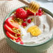 A bowl of dairy-free vanilla chamomile coconut yogurt alternative topped with sliced strawberries, raspberries, pomegranate seeds, chopped pistachios, and a drizzle of honey.