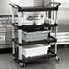 A black Rubbermaid Xtra cart with dishes and cups on a tray.