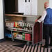 A large portable bar with a red maple laminate finish, stainless steel top, fixed speed rail, and two ice bins, stocked with beverages and mixers.
