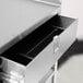 A stainless steel equipment stand with an open drawer, featuring three shelves and casters.