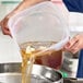 A translucent round polypropylene food storage container being used to pour liquid with ingredients into a strainer.