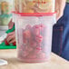 A translucent round polypropylene food storage container with a red lid, filled with strawberries and marked with quart measurements.
