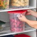 A translucent round polypropylene food storage container with a red lid, filled with strawberries and labeled with measurement markings.