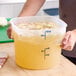 A large translucent round polypropylene food storage container with measurement markings, filled with liquid and vegetables.