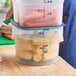 A translucent round polypropylene food storage container filled with corn on the cob, with measurement markings on the side.