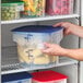A translucent round polypropylene food storage container with a blue lid, filled with corn on the cob and marked with volume measurements.
